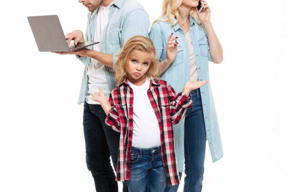 Full length portrait of a busy family talking on mobile phone and using laptop with a child standing and shrugging shoulders isolated over white background
