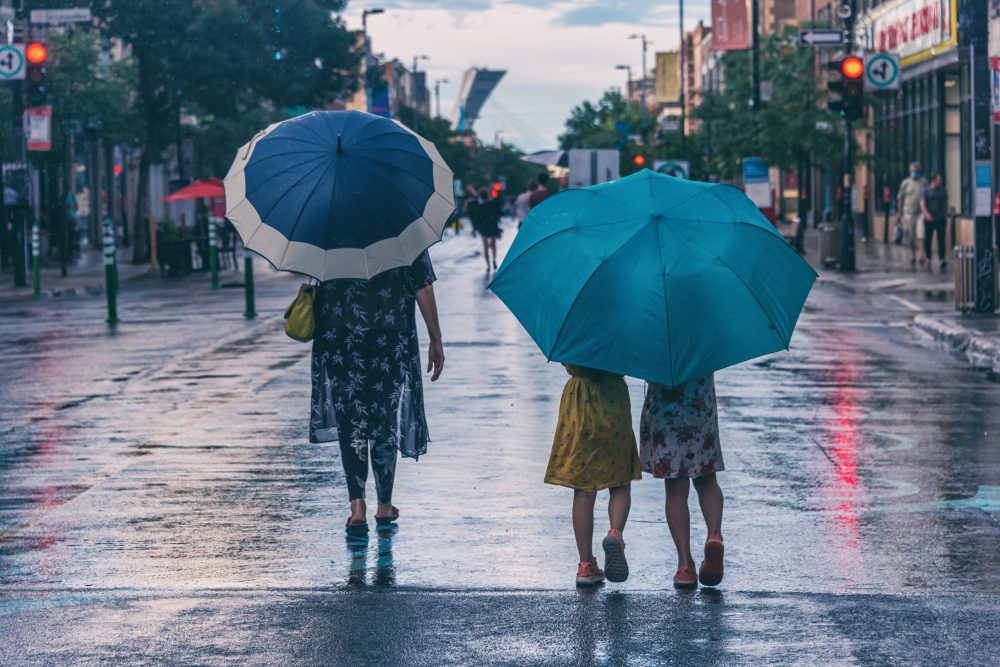 Montreal, CA - 30 July 2020: Mother and daughters on Mont-Royal Avenue holding umbrellas during rain & storm