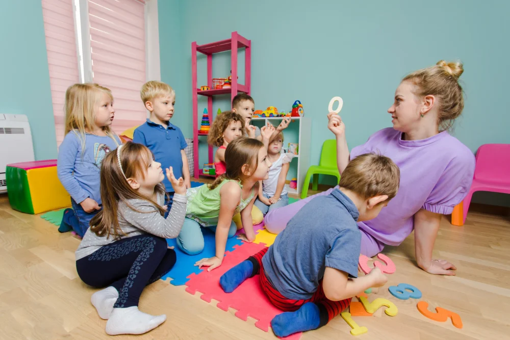 attractive-preschool-teacher-teaching-group-lovely-children-sitting-floor-kindergarten-preschool-young-learners-are-very-relaxed-engaged-while-lesson